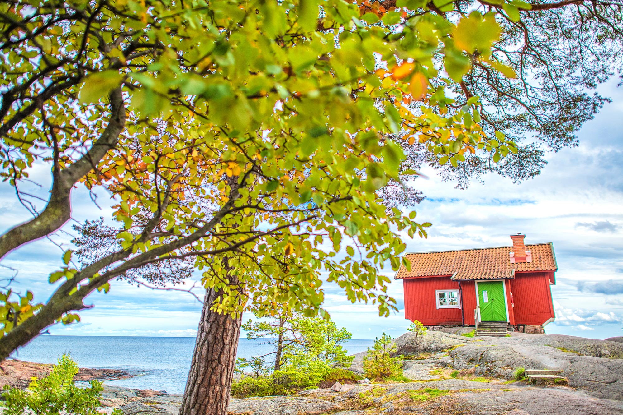 A red house with a green door perched on a cliff overlooking the water